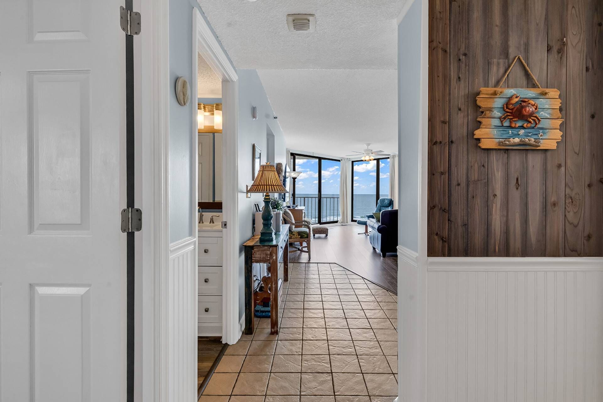 Ein Flur, der zu einem Balkon mit Meerblick führt, eine Holzwand mit einer Dekoration einer Krabbe und ein Deckenventilator.