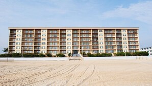 A multi-story hotel with a uniform facade, balconies, and a sandy beach in the foreground. - Adorable, spacious 2-bedroom oceanfront condo with free WiFi and a fabulous ocean view located directly on the Boardwalk! (Ocean City)