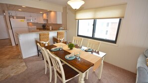 A dining area with a wooden table, white chairs, and a view of the kitchen. - Adorable, spacious 2-bedroom oceanfront condo with free WiFi and a fabulous ocean view located directly on the Boardwalk! (Ocean City)