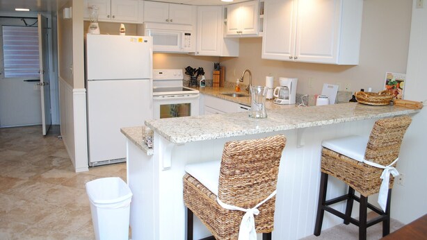 A modern kitchen with white cabinets, a granite countertop, and two wicker bar stools. - Adorable, spacious 2-bedroom oceanfront condo with free WiFi and a fabulous ocean view located directly on the Boardwalk! (Ocean City)