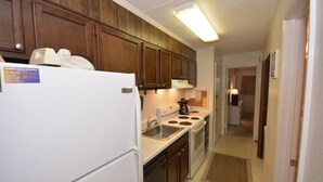 Una cocina compacta con armarios de madera, un refrigerador blanco, una estufa y un lavamanos.