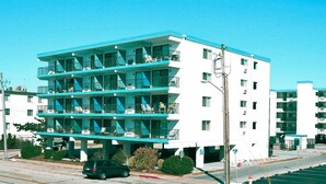 Un hotel de varios pisos con balcones en cada planta, un estacionamiento al frente y un cielo azul despejado.