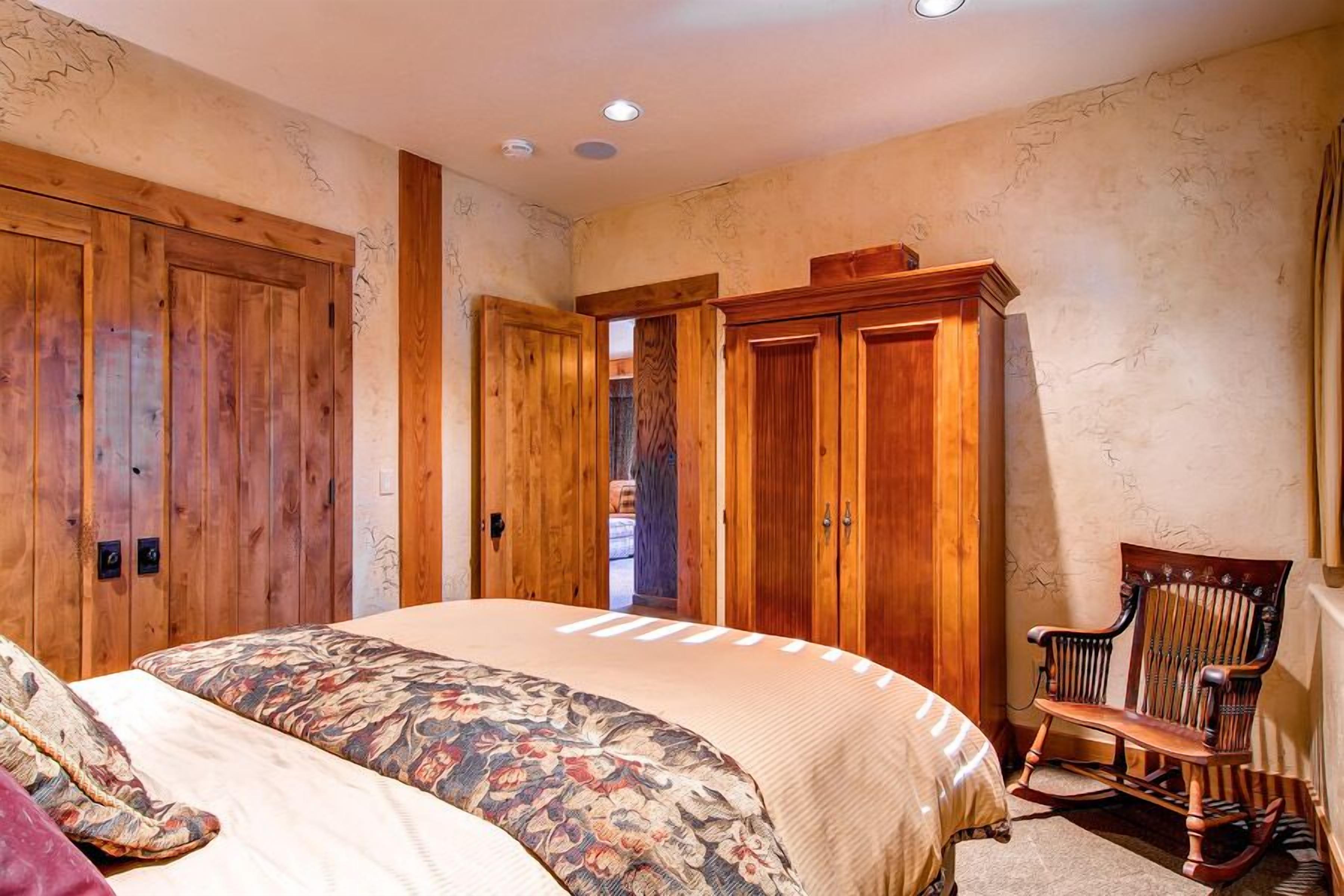 A bedroom with a large bed, wooden wardrobe, and a rocking chair.
