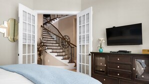 Quarto com cama, penteadeira, televisão e escada que dá para outro cômodo.