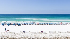 Ein Strand mit Reihen von Sonnenschirmen und Liegestühlen, ein sandiger Uferstreifen und das Meer im Hintergrund.