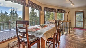 A dining area with a table set for four, large windows with curtains, a wooden deck outside, and a view of trees. - 3 Mi to Ski Slopes! Hot Tub Haven in Breckenridge (Breckenridge)