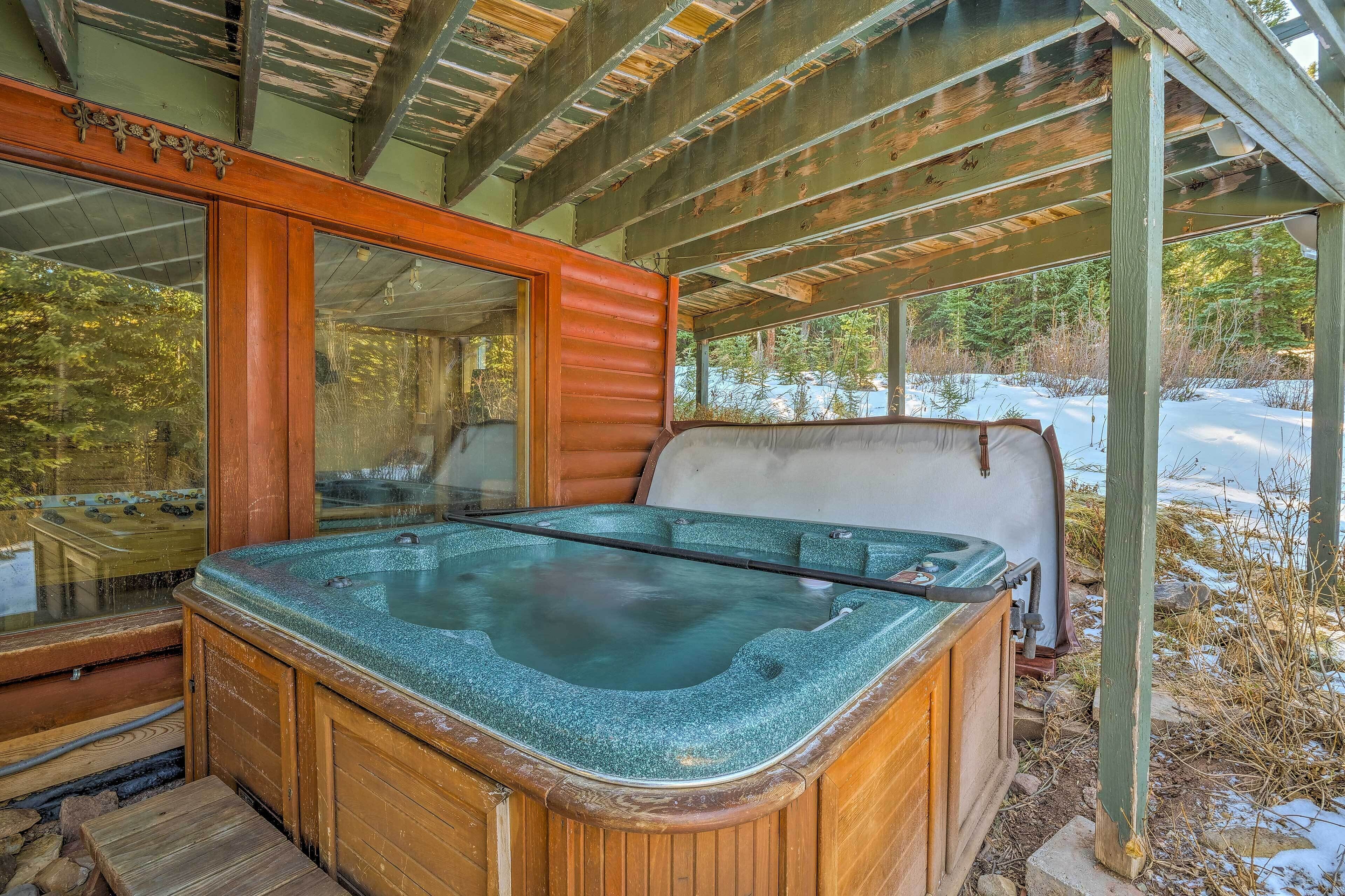Una bañera de hidromasaje de madera con recinto de vidrio, rodeada por una rústica cabaña con techo de metal.
