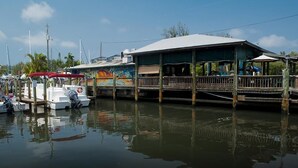 Een restaurant aan het water met een overdekt terras, boten afgemeerd in de buurt, en een muurschildering op het gebouw.