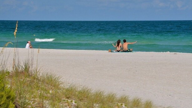 Een strand met helder uitzicht op de oceaan en een persoon die op het zand zit.