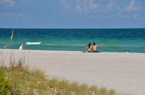A beach with a clear view of the ocean and a person sitting on the sand.