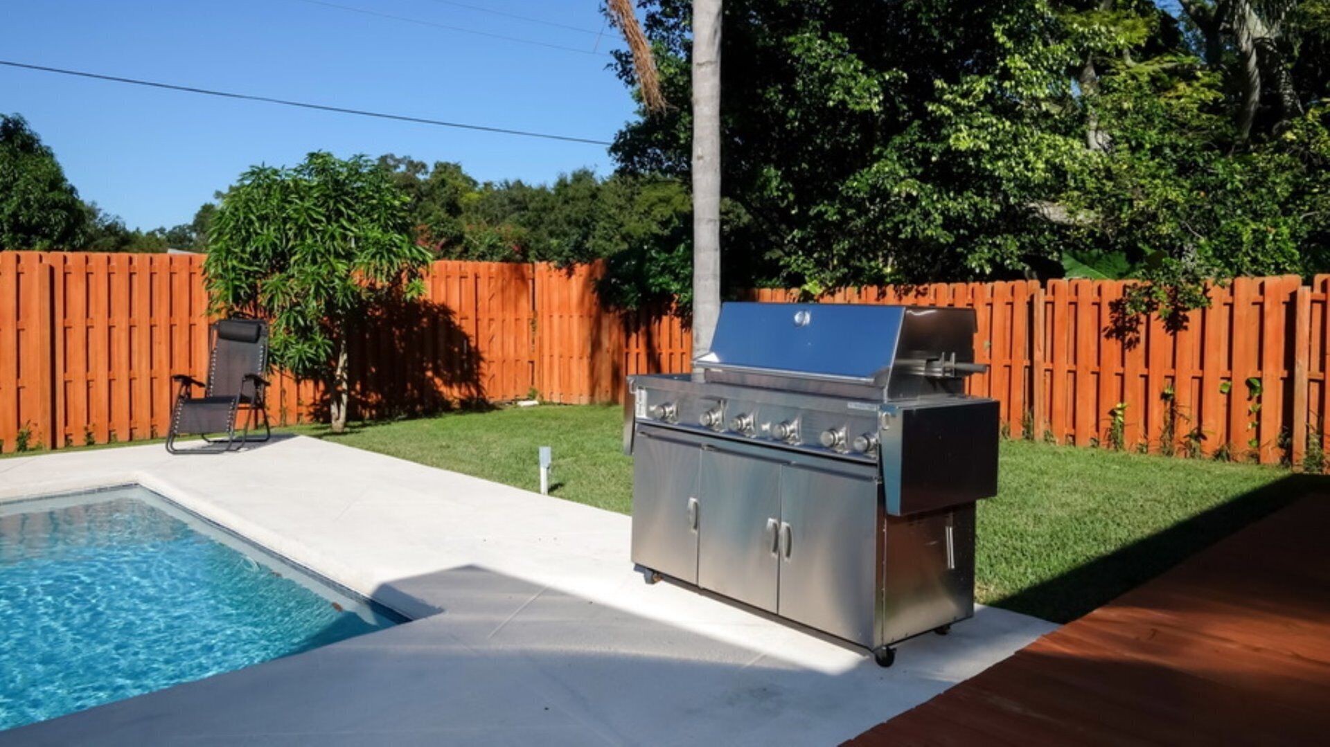 A backyard with a swimming pool, a barbecue grill, and a wooden fence.