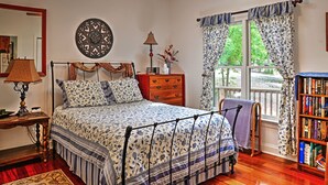 A bedroom with a bed, a nightstand, a lamp, a wooden dresser, a window with curtains, and a bookshelf. - Cozy Scottsville Cottage w/ River Views & Gazebo! (Scottsville)