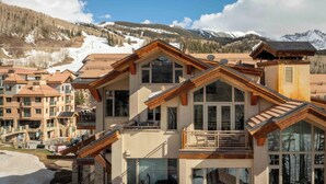 A multi-story hotel with large windows, wooden balconies, and a ski slope in the background.