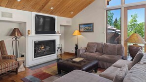 A living room with a fireplace, a sofa set, a lamp, and a view through large windows.