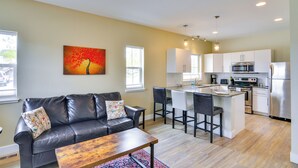 Una cocina moderna con electrodomésticos de acero inoxidable, un comedor con taburetes de bar y una sala de estar con un sofá de cuero y una mesa de centro.