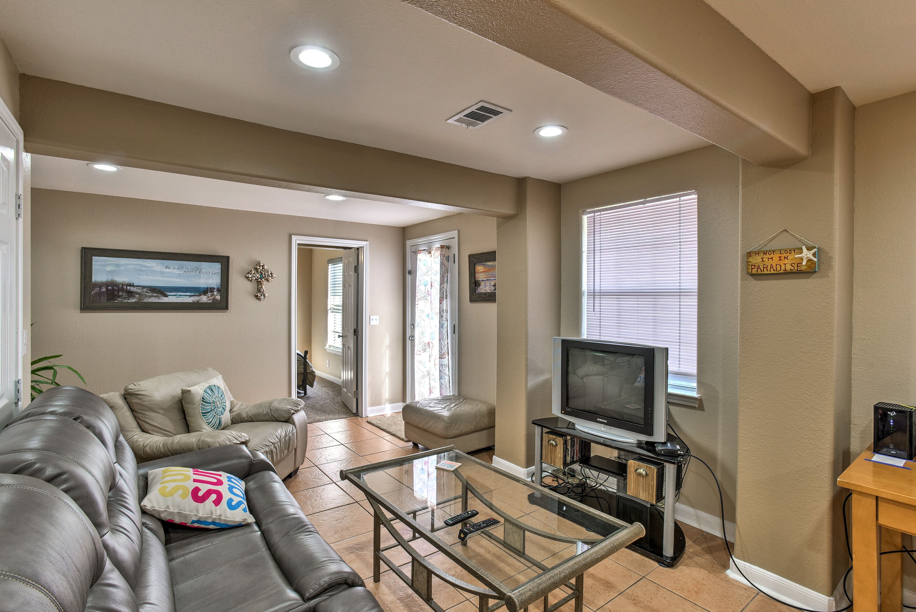 A living room with a leather sofa, a glass coffee table, a television, and a bookshelf.