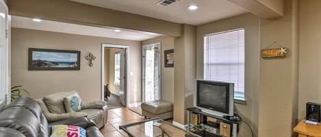 A living room with a leather sofa, a glass coffee table, a television, and a bookshelf.