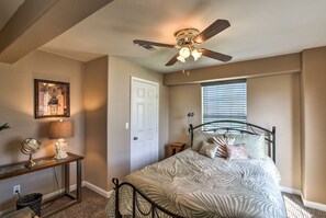 Une chambre à coucher comprenant un lit, un ventilateur de plafond, une table de chevet avec une lampe, un miroir et une fenêtre avec des stores.