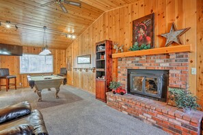 A cozy room with a pool table, leather couch, fireplace, and wooden walls.
