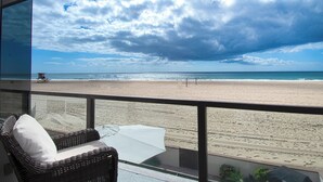 Une vue sur la plage depuis un balcon, avec une chaise en osier et une table.