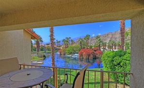 A balcony with a view of a water feature, palm trees, and a mountain in the background.