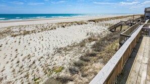 A beach with a wooden boardwalk leading to a building. - Queen's Grant D-113 – Ocean Views & Beach Fun (Topsail Beach)