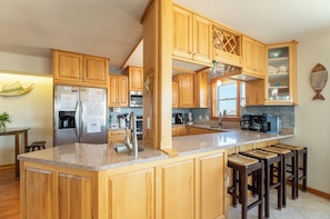 A kitchen with wooden cabinets, stainless steel appliances, a granite countertop, and a bar area with stools.