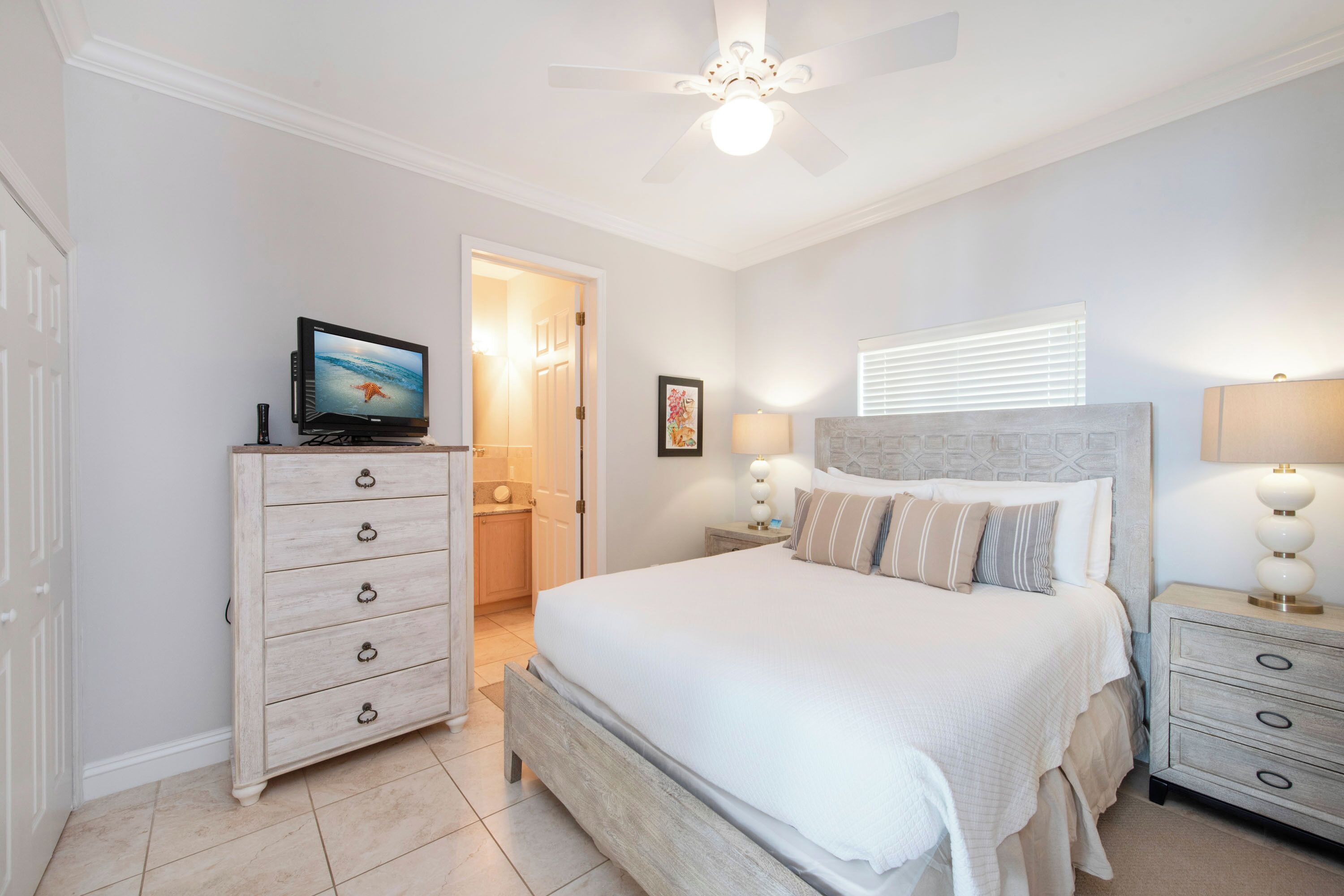Quarto com cama, penteadeira, televisão e ventoinha no teto.