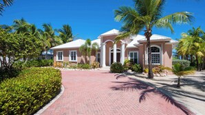 A two-story building with a pink facade and white trim, surrounded by palm trees and a brick pathway.
