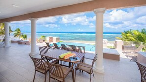 A covered outdoor area with a table and chairs, a pool, and a view of the ocean.
