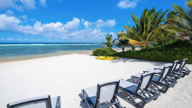 A beach with white sand, a row of sun loungers, and a clear blue sky.
