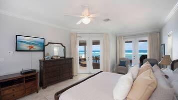 A bedroom with a large bed, a dresser, a television, and a view of the ocean through the door.