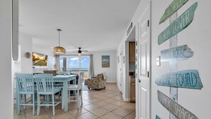 Uma sala de jantar ampla com vista para o oceano, uma cozinha com uma janela grande e um corredor com placas de sinalização.