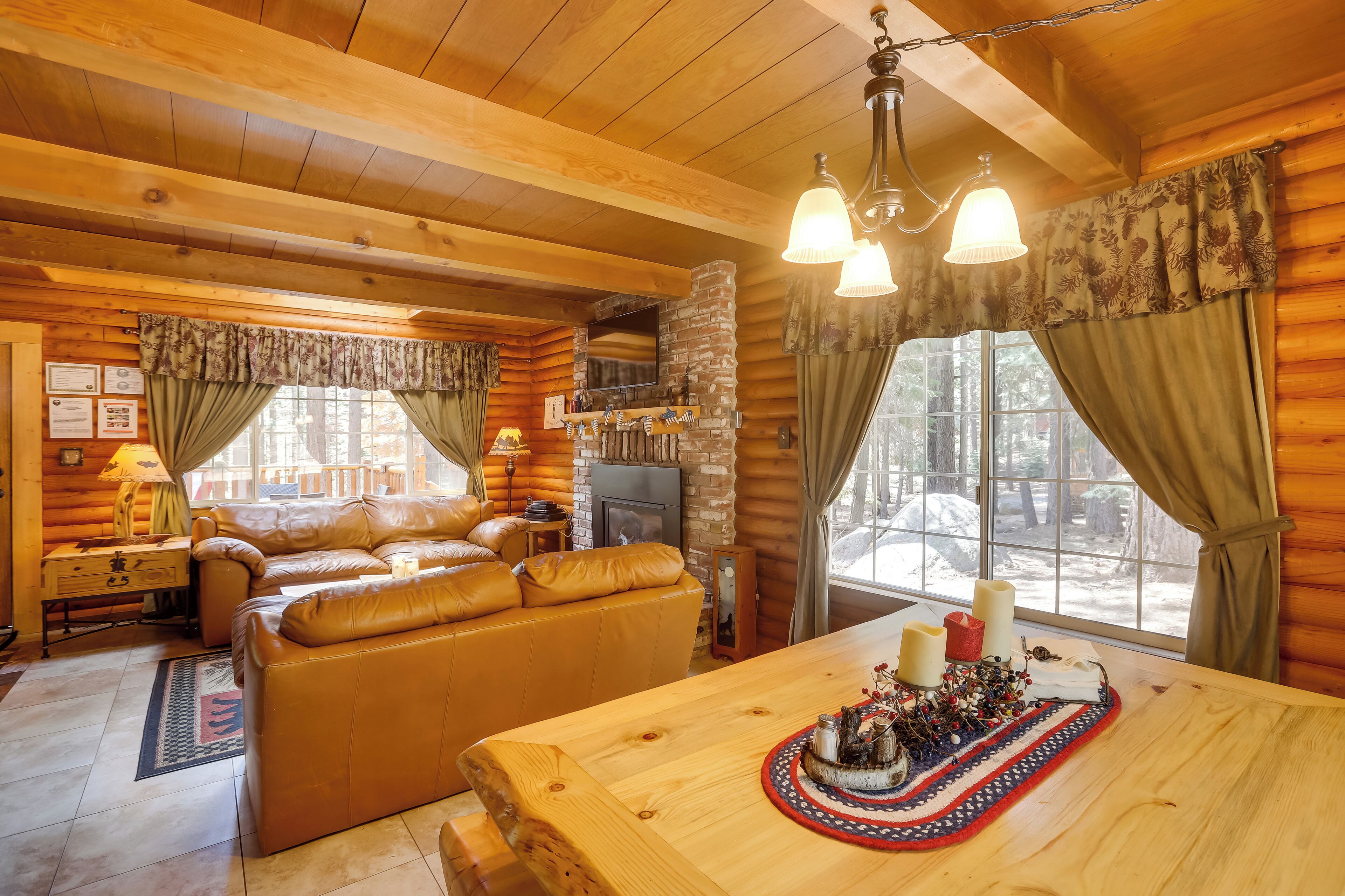 Ein gemütliches Blockhaus-Interieur mit Kamin, Ledersofa, Holzesstisch und großen Fenstern.