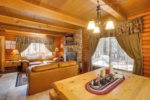 Ein gemütliches Blockhaus-Interieur mit Kamin, Ledersofa, Holzesstisch und großen Fenstern.