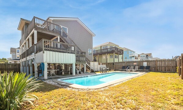 A two-story house with a backyard swimming pool, a wooden deck, and a fenced area. - 3 Little Gulls - Corolla, Ocean Sands, 30 Ft to Beach, Semi-Oceanfront, Pool, Hot Tub, Pets OK (Corolla)