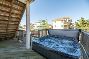 A wooden deck with a hot tub, wooden railings, and a view of multi-story buildings in the background. - 3 Little Gulls - Corolla, Ocean Sands, 30 Ft to Beach, Semi-Oceanfront, Pool, Hot Tub, Pets OK (Corolla)