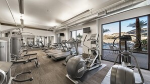 Une salle de sport moderne équipée de machines de cardio, de postes de musculation et de grandes fenêtres donnant sur une piscine et des palmiers.