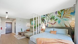 Une chambre moderne avec un grand lit, un canapé, une table à manger et une fresque représentant des feuilles tropicales sur le mur.