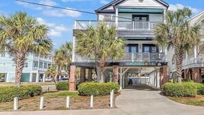 A two-story building with a balcony on the upper floor, a sign reading "Sunsational Tara," and palm trees in the foreground. - Beautiful, clean and spacious dog friendly beach home! Special summer rates! (SURFSIDE BEACH)