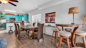 A modern kitchen with teal cabinets, a dining area with wicker chairs, and a large painting on the wall. - Beautiful, clean and spacious dog friendly beach home! Special summer rates! (SURFSIDE BEACH)
