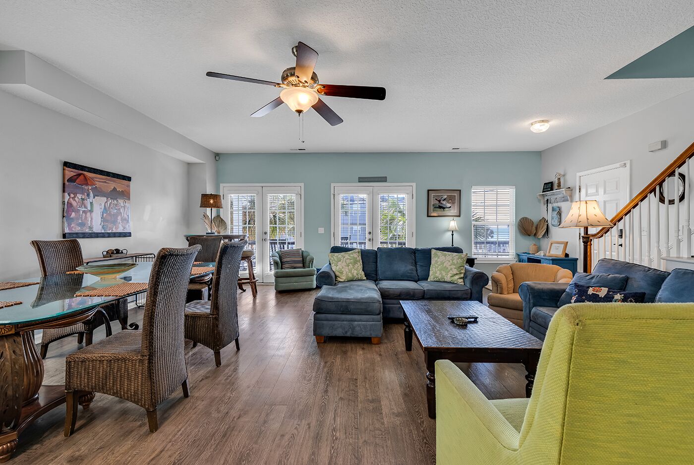 A spacious living room with a glass dining table, comfortable seating, and a ceiling fan.
