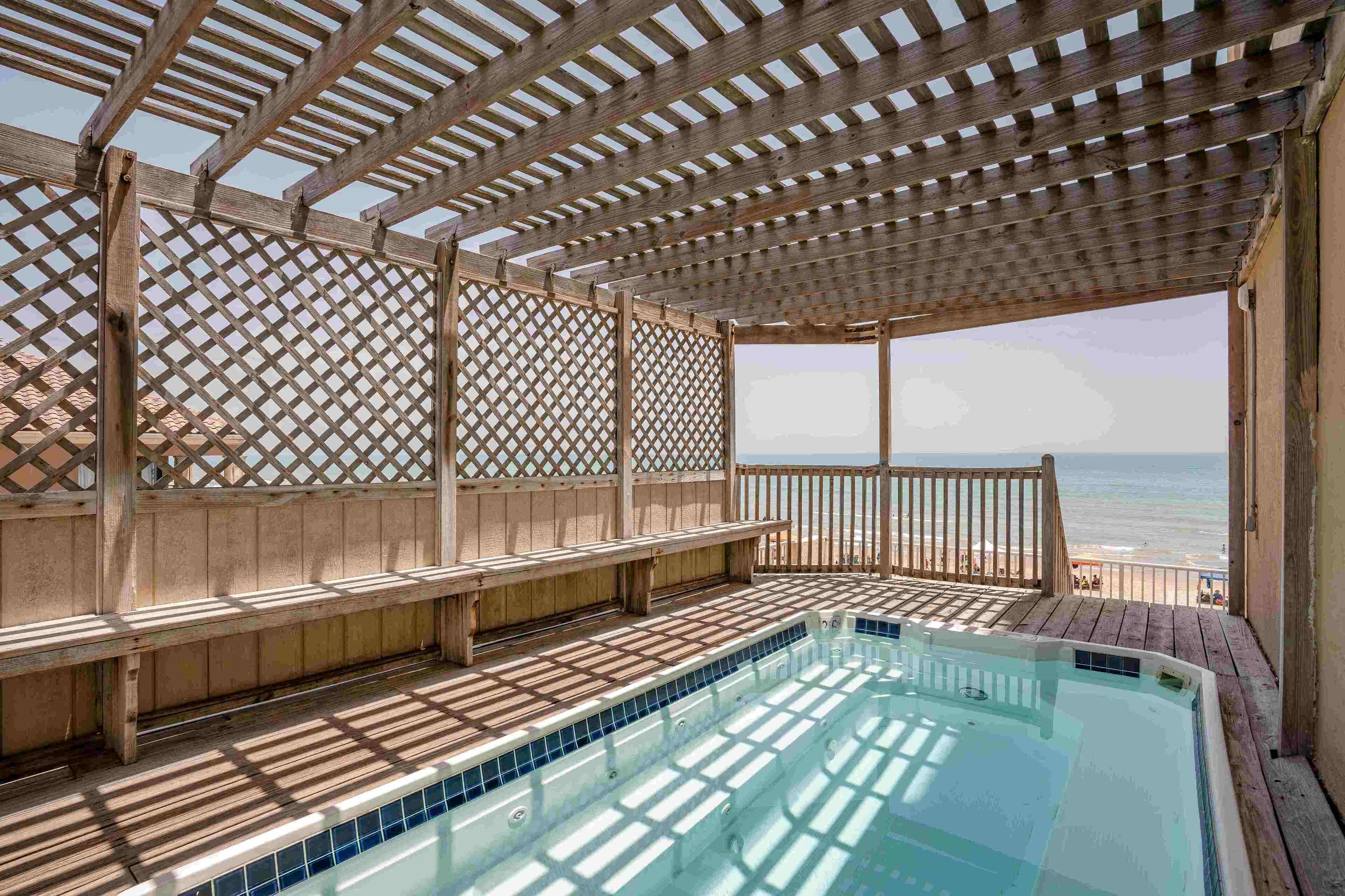 Une terrasse en bois avec une piscine, donnant sur une plage.
