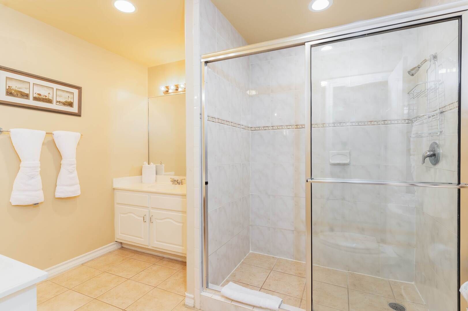 Un baño con ducha de vidrio, tocador con espejo y dos toallas blancas colgadas en la pared.