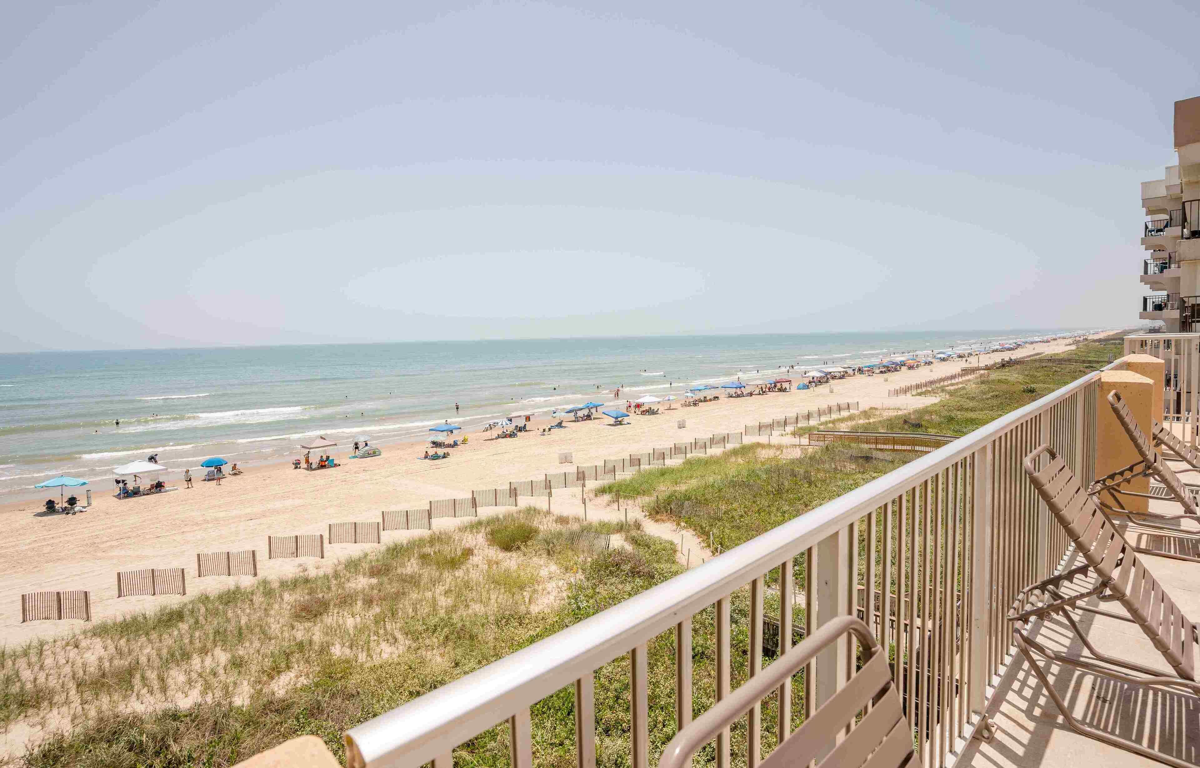 Blick auf einen Strand von einem Balkon mit Geländer, Strandstühlen und Sonnenschirmen.