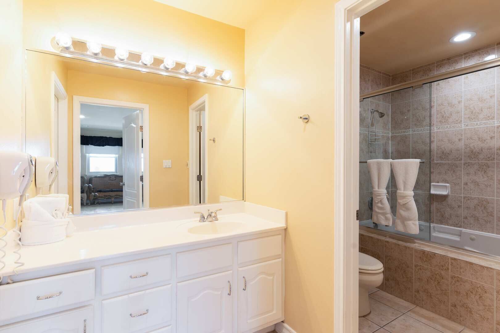 A bathroom with a large mirror, vanity with a sink, and a shower area.