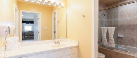 A bathroom with a large mirror, vanity with a sink, and a shower area.