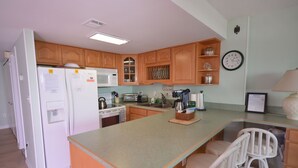 Una cocina con gabinetes de madera, un refrigerador, un microondas, una estufa, un fregadero y una zona de bar con taburetes.