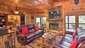 Interior acogedor de una cabaña con sofá de cuero, rincón para café, chimenea y televisor.