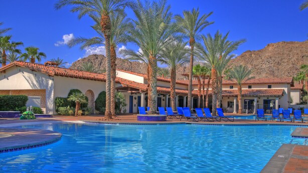 A pool area with blue lounge chairs, palm trees, and a mountain backdrop.
